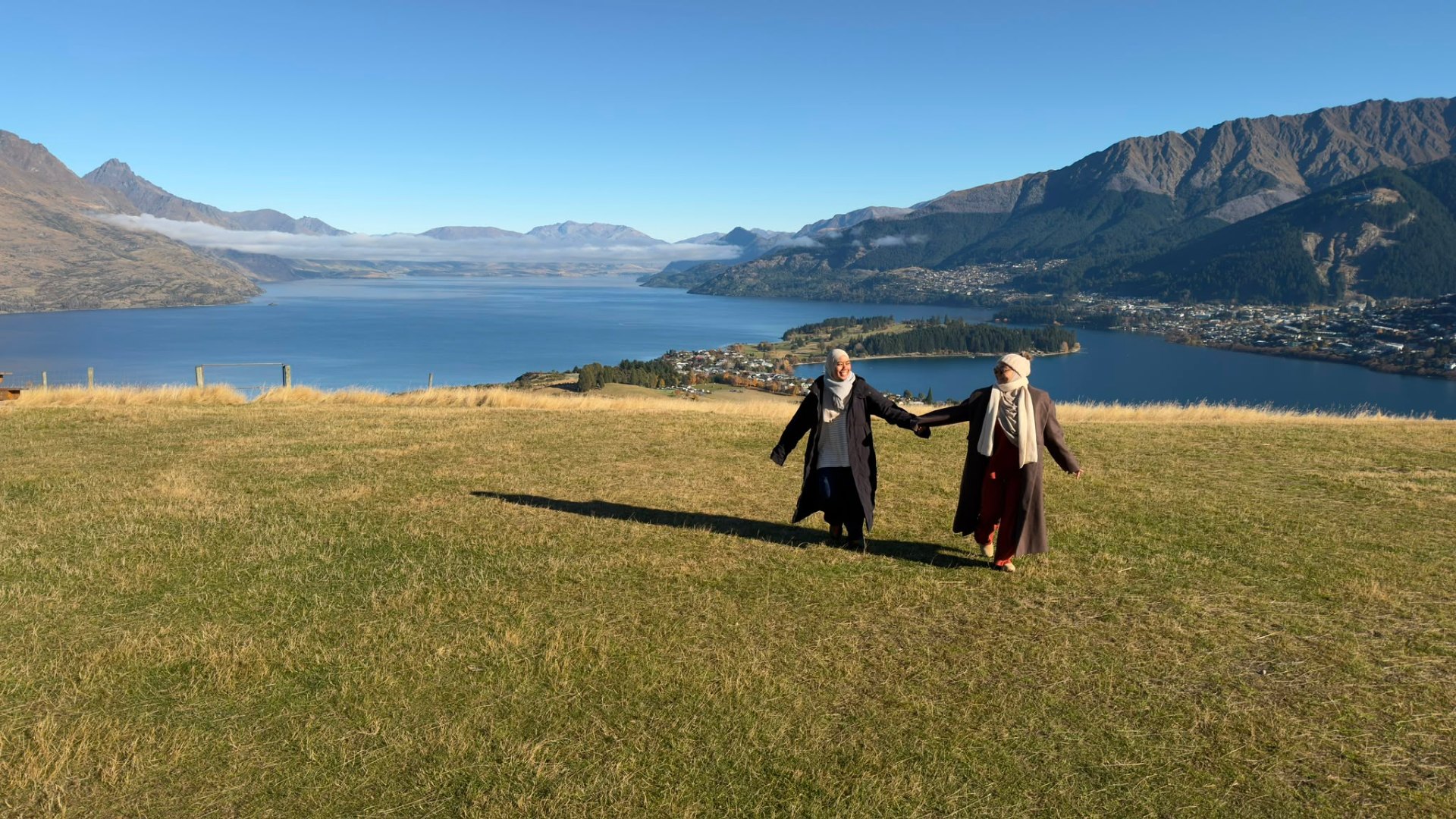 Humairah and Sakinah walking hand-in-hand on a hillside overlooking a lake