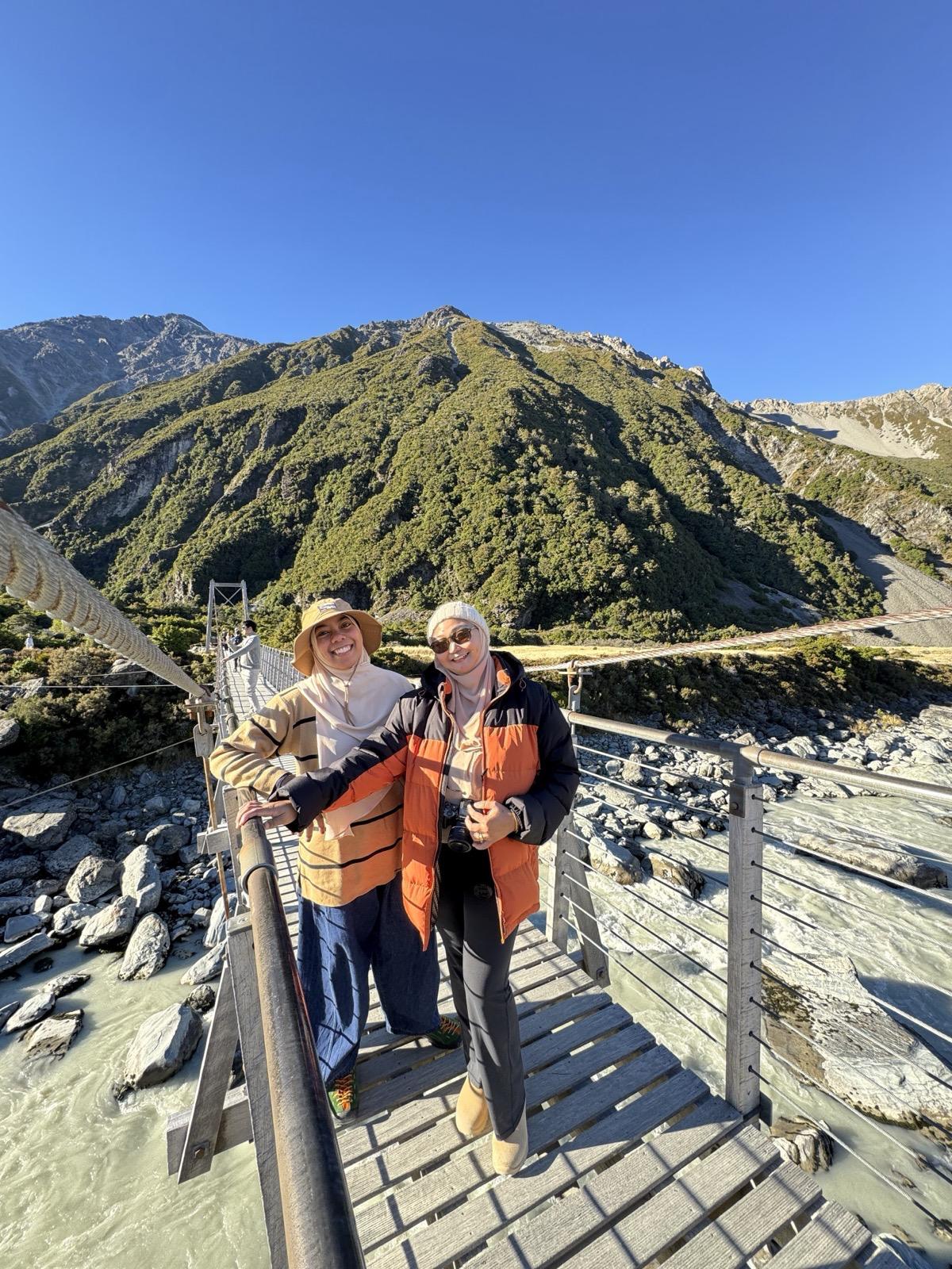 Humairah and Sakinah smiling on a suspension bridge with mountains behind them